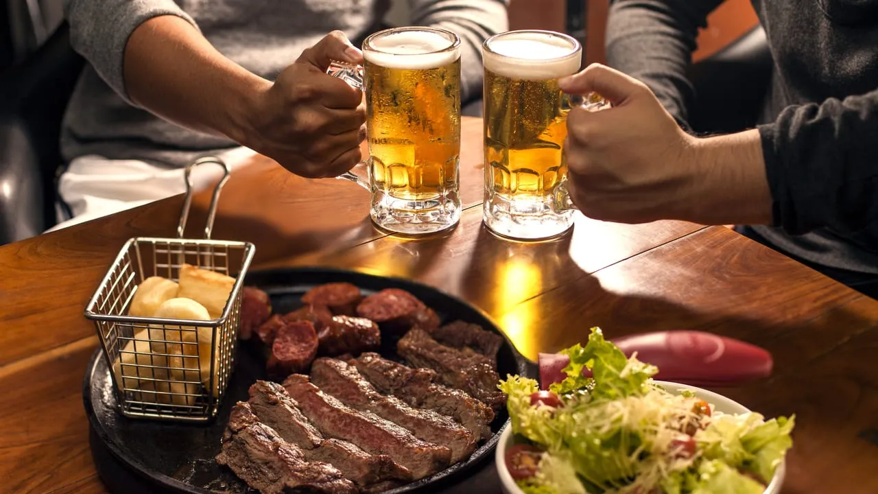 Amigos brindando com canecas de chope sobre mesa com petiscos